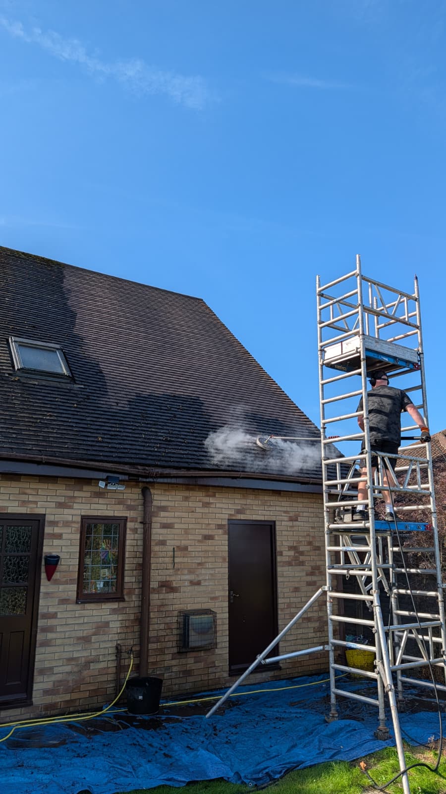 A roof being steam cleaned in Boston, by a man on a scaffold tower. 
